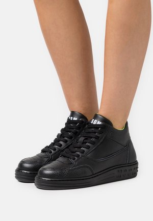 Baskets montantes noires avec détails en cuir texturé, lacets noirs et logo "MSGM" sur la languette et la semelle, portées sur des jambes nues.