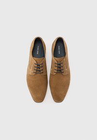 Zapatos de ante marrón con cordones, diseño de punta afilada, con cordones y forro interior de color azul oscuro, textura suave y detalles mínimos.