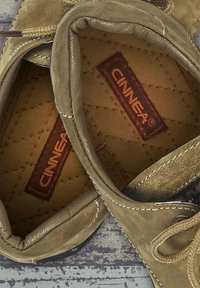 Beige leather shoes with a soft texture, rounded shape, and stitched detailing. Interior has a quilted pattern and logo on the insole.