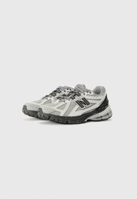 Chaussures de sport avec une tige en maille grise et noire, accents blancs, semelle en caoutchouc noir robuste et détails texturés sur les orteils.