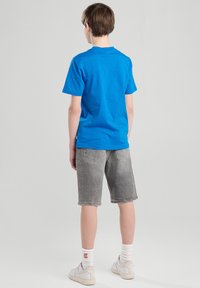 Sininen puuvillapaita, lyhyt hiha, yhdistetty harmaisiin farkkushortseihin. Yksinkertainen malli, pyöreä kaula-aukko, käytetty valkoisten tennareiden ja sukkien kanssa.