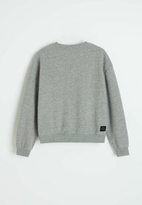 Szara bluza z luźnym krojem, prążkowanym okrągłym dekoltem i mankietami. Wyrazisty czarny akcent z metką blisko dołu. Miękka, teksturowana tkanina.