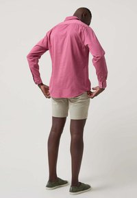 Camisa rosa de manga corta con cuello abotonado, combinada con pantalones cortos beige claro y zapatillas verdes; tejido liso sin patrones visibles.