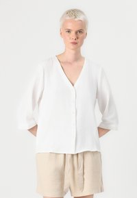 White, V-neck blouse with three-quarter sleeves and button closure, made of lightweight fabric, featuring a relaxed fit and subtle texture.