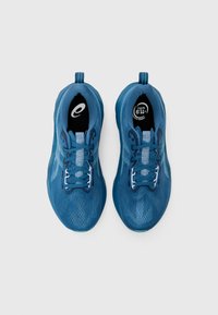 Baskets de sport bleues avec une tige en maille, bout arrondi et lacets contrastants. Présente un logo sur la languette et une semelle texturée.