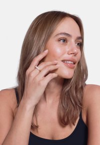 Ein Gold- und Perlenring an einer Hand, mit einem glatten goldenen Band und drei weißen Perlen, präsentiert an einem Model mit langen, glatten Haaren.