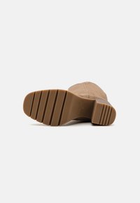 Botte en cuir marron avec une tige texturée, un talon bloc et une semelle en caoutchouc striée avec des crans horizontaux pour une meilleure traction.