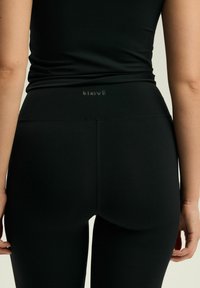 Czarne legginsy o gładkiej strukturze, z wysokim stanem i subtelnym logo z tyłu. Dopasowany krój podkreśla smukłą sylwetkę.