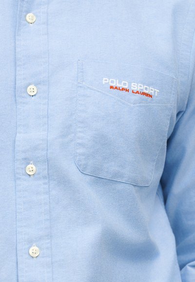 Ανοιχτό μπλε πουκάμισο με τσέπη στο στήθος κεντημένη με το "POLO SPORT RALPH LAUREN" σε λευκό και κόκκινο κλωστή.