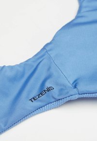 Modrý látkový podprsenka s hladkým povrchem, elastickými okraji a tištěným černým logem, s bezproblémovým designem pro pohodlí a dobré padnutí.