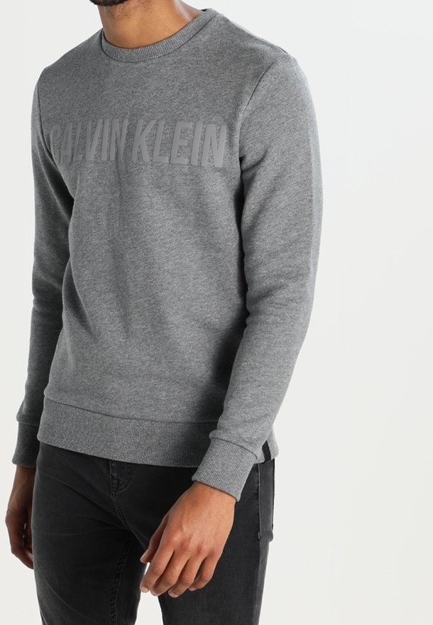 Sudadera gris con cuello redondo, puños y dobladillo acanalados, que presenta un destacado logo de Calvin Klein en un tono más oscuro en el pecho.