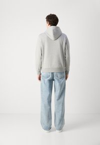 Grå hettegenser med avslappet passform, sammen med lyseblå vide jeans. Enkelt design, myk tekstur og ribbestrikkede mansjetter.