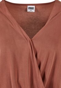 Hnedo-oranžový obalový top z ľahkej, hladkej tkaniny s hlbokým výstrihom do V, ktorý obsahuje detail twist v strede a jemné prešitie.