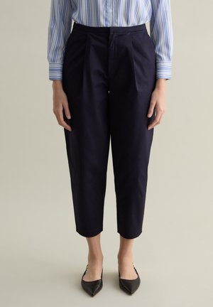 Pantaloni a culotte blu navy con pieghe, realizzati in un tessuto liscio. Indossati con una camicia a righe blu e bianca e ballerine nere a punta.