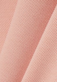 Gros plan sur un tissu tricoté doux de couleur rose clair, montrant une texture détaillée et un motif de couture fine.