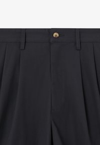 Pantaloni blu scuro con una texture liscia, caratterizzati da pieghe doppie, un bottone marrone e una vita con passanti per la cintura.