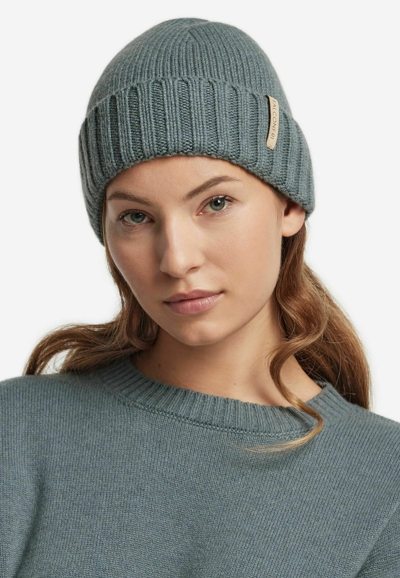 Grå stickad mössa med vertikal ribbning, med en sydd etikett. Modellen bär en matchande grå tröja med rund halsringning.