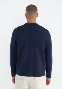 Marinblauer Strickpullover mit umschlagbarem Kragen und langen Ärmeln. Hat ein strukturiertes Finish. Kombiniert mit hellen Cargo-Hosen.