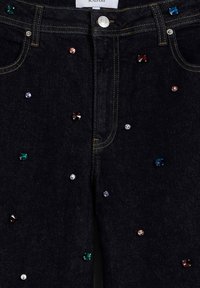 Pantalones vaqueros de mezclilla oscura con adornos dispersos de varios diamantes de imitación coloridos y herrajes metálicos, enfatizando los bolsillos y las costuras.