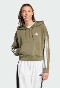 Oliivinvihreä lyhyt huppari, jossa on etutasku, neljännes-vetoketju ja valkoinen Adidas-logo. Hihassa valkoiset raidat. Pehmeä kangas.