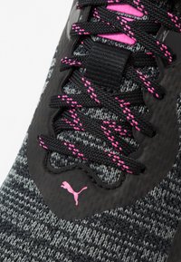 Tige de chaussure de sport tricotée noire et grise avec des lacets et des accents roses. Présente un motif texturé et un logo sur le côté.