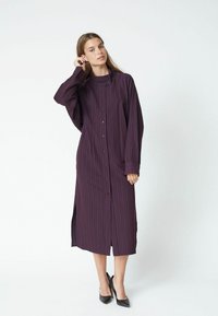 Long, button-up shirt dress in dark purple with vertical stripes, featuring long sleeves, side slits, and a structured collar.