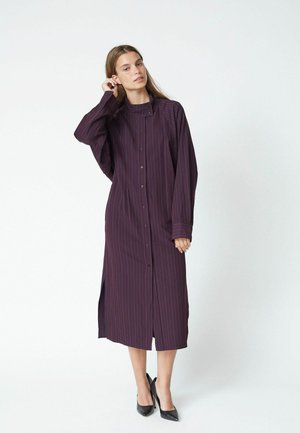 Lungo vestito camicia a bottoni di colore viola scuro con righe verticali, dotato di maniche lunghe, spacchi laterali e un colletto strutturato.
