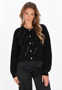 Cardigan nero a maglia con una texture a coste, caratterizzato da motivi diagonali di paillettes argento e ampi bottoni tondeggianti sulla parte anteriore.