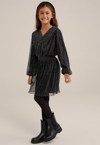 Svart vikt klänning med långa ärmar, V-ringning och smockad midja, tillsammans med svarta ankboots och prickiga svarta strumpbyxor.