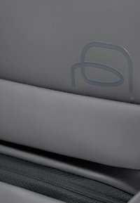 Grauer Stoff mit glatter Textur und einem dezenten geprägten Muster; ein schwarzer Reißverschluss ist am unteren Rand teilweise sichtbar.