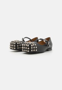 Zapatos de cuero negro con suela plana, que cuentan con una correa y múltiples tachuelas metálicas plateadas en la parte del dedo. Textura suave con acentos redondeados.