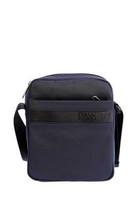 Bolso cruzado compacto en azul marino con correa negra y bolsillo delantero con cremallera, que presenta una tira con el logotipo en relieve "coronel tapiocca".