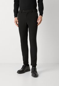 Czarne, dopasowane spodnie o gładkiej fakturze, z zapięciem na guzik, szlufkami na pasek i bocznymi kieszeniami, zestawione z czarnymi butami.