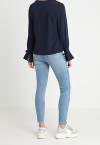 Námornická blůza s dlouhými rukávy a stahovacími šňůrkami na manžetách, zkombinovaná se světlými modrými skinny džíny a teniskami se stříbrnými detaily.