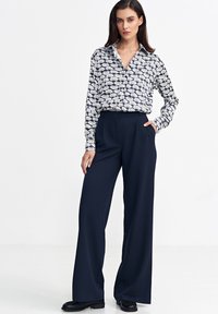 Koszula na guziki w czarno-białym wzorze muszli, zestawiona z granatowymi spodniami o szerokich nogawkach. Tkanina wydaje się gładka; spodnie mają boczne kieszenie.