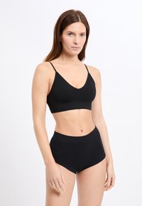 Schwarzer Sport-BH und hoch taillierte Shorts mit texturiertem Muster und verstellbaren Trägern. Das Material wirkt glatt und dehnbar.