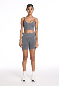 Szary sportowy crop top i pasujące szorty wykonane z teksturowanej tkaniny, z bocznym logo. Modelka ma na sobie białe sneakersy z skarpetkami do kostek.