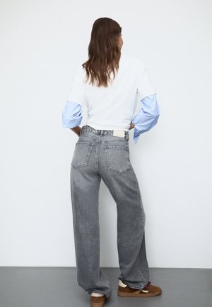 Jean gris à jambes larges avec une taille haute, doté de poches arrière et d'une étiquette. Associé à une chemise blanche à rayures bleues, style décontracté.