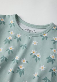 Groen shirt met korte mouwen, versierd met een bloemmotief van witte bloemen met gele centra en groene bladeren. Zacht katoenen materiaal met een ronde hals.