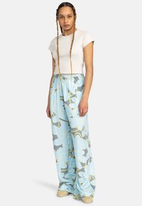 Pantalons larges à motifs bleus clairs avec des designs floraux et une taille élastique, associés à un haut ajusté à manches courtes crème.