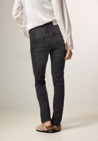 Jeans de mezclilla negros ajustados, con bolsillos traseros y un lavado sutil. Combinados con zuecos beige, modelados desde la parte de atrás.