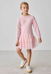 Ružové šaty s dlhými rukávmi, textúrovaným úpletovým živôtikom a viacvrstvovou tylovou sukňou. Na hrudi je zlatá výšivka a nosia sa s bielymi topánkami.