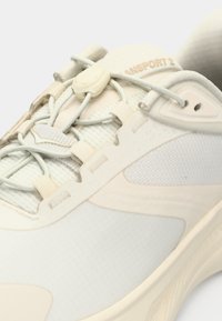 Ανοιχτό μπεζ αθλητικό παπούτσι με πλεκτό ύφασμα, κορδόνια γρήγορης δέσης και μαλακή σόλα, με κοντινή όψη από το πλάι και πάνω.