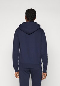 Marineblå hettegenser laget av myk stoff, med en stor hette, ribbede mansjetter og liv. Enkelt design uten synlige logoer eller mønstre.