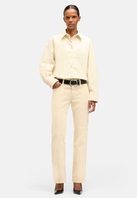 Camicia crema con bottoni e maniche oversize, abbinata a pantaloni dritti beige chiaro e una cintura nera con fibbia in argento.