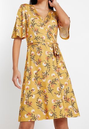 Omslagskjole i gult stof med blomsterprint i pink og hvid. Har korte flagrende ærmer og bindebånd i taljen for en tætsiddende silhuet.