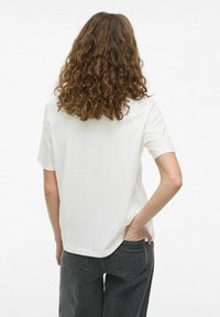 Camiseta blanca de manga corta con un corte holgado y escote redondo, combinada con jeans de tiro alto en gris oscuro.