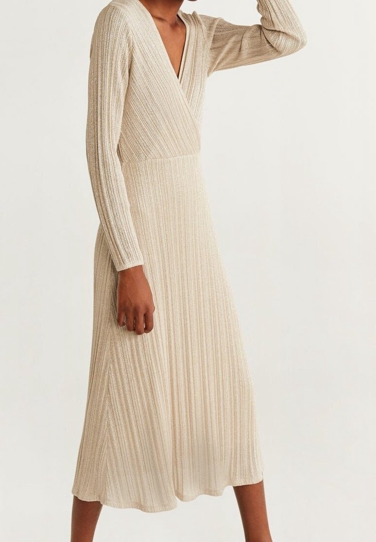 Femme portant une robe midi en maille côtelée beige à manches longues, avec un col en V et une taille cintrée, debout devant un fond clair uni.