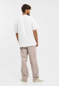 Biela bavlnená tričko s krátkymi rukávmi, voľný strih, viditeľné švy, skombinované so svetlými béžovými nohavicami a svetlými teniskami.