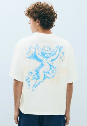 Young person with curly hair wearing a white shirt featuring a blue cherub holding a banner that reads "The winners ascend."
